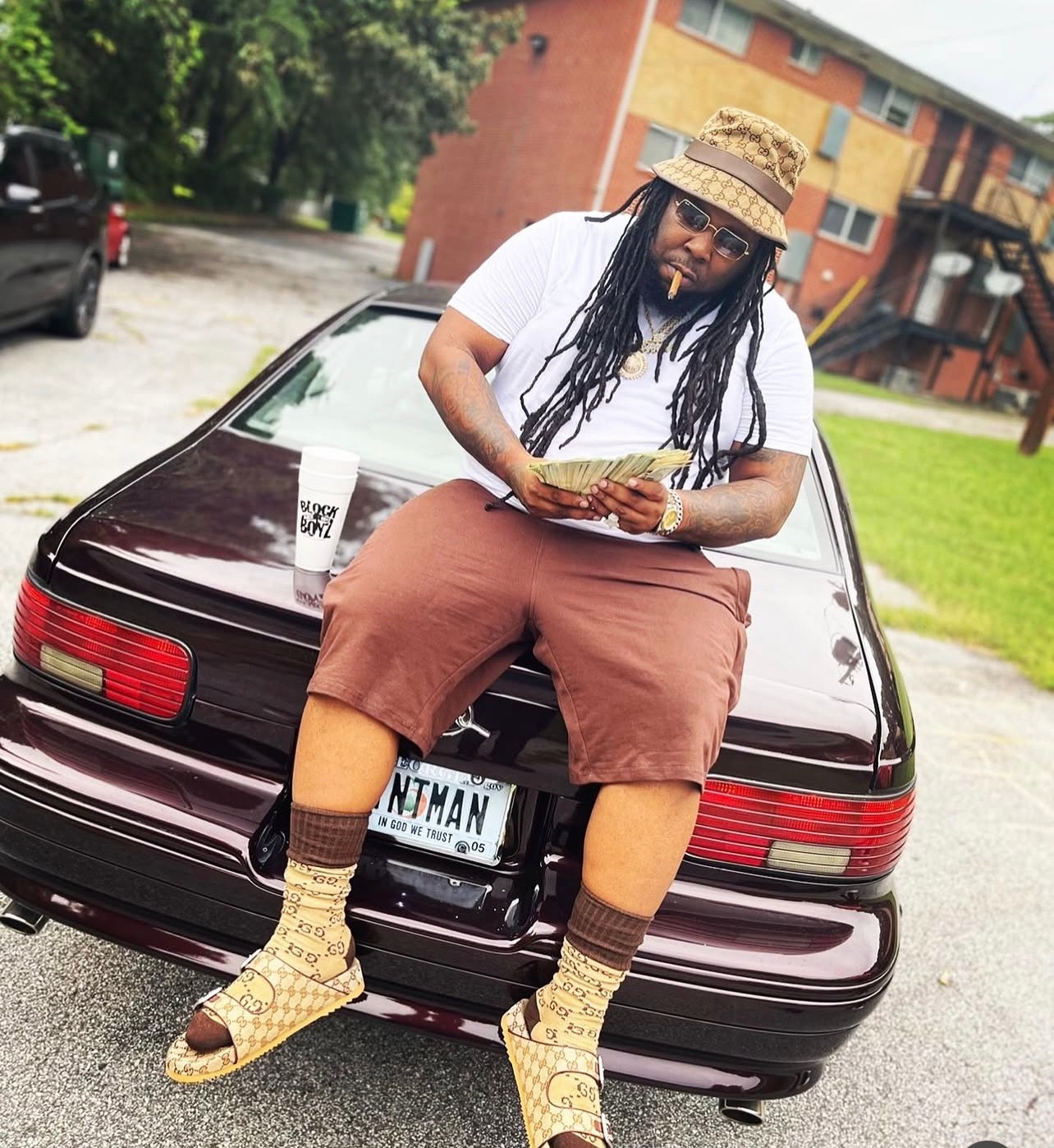 Blockboy Spanky sitting on the trunk of a burgundy Caprice holding cash