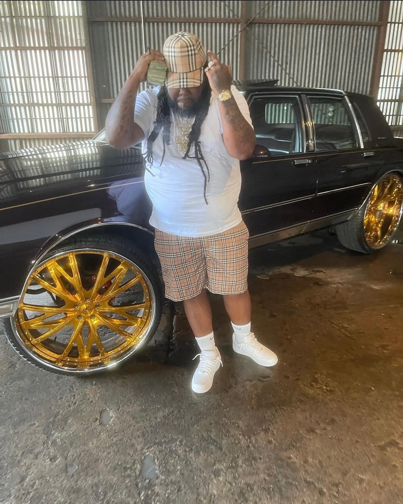 Blockboy Spanky posted up beside a black box Chevy on gold rims